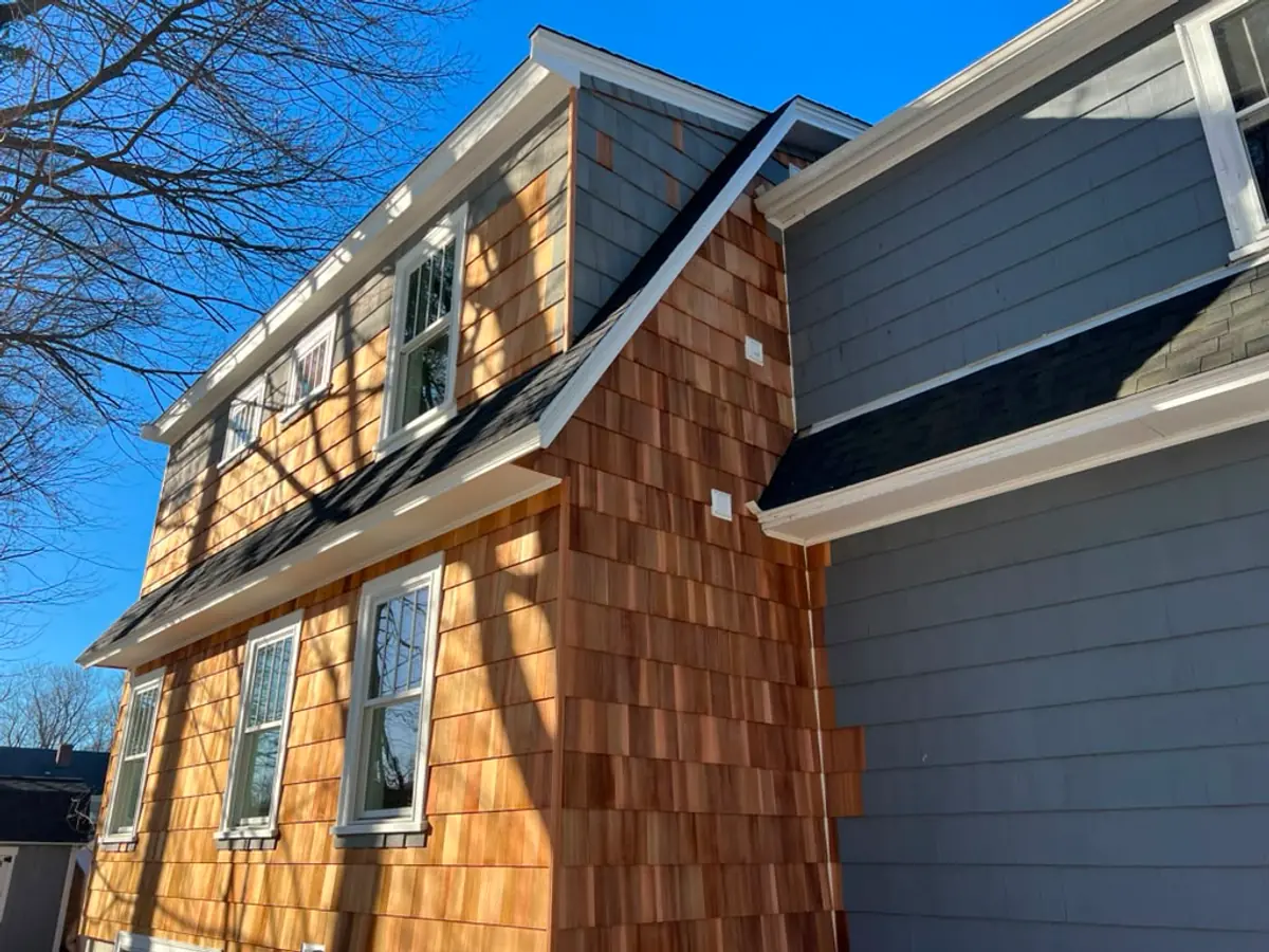 New cedar shingle siding meeting the original grey clapboard on a Reading, MA home